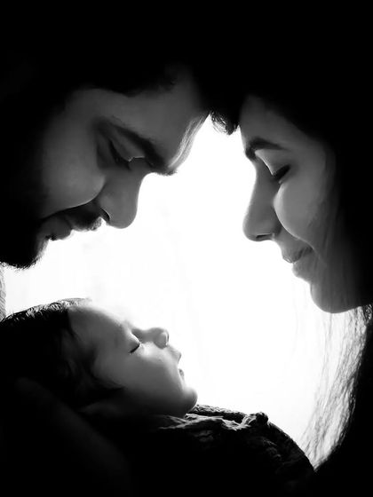 A beautiful black and white portrait of a new family. The rim lighting creates a powerful and emotional silhouette, highlighting their bond with their newborn.