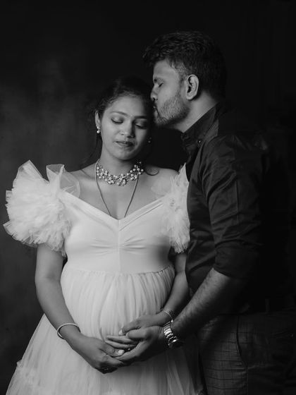 An artistic black-and-white studio portrait. The soft lighting and tender pose, with the partner kissing her forehead, create a timeless and emotional image.