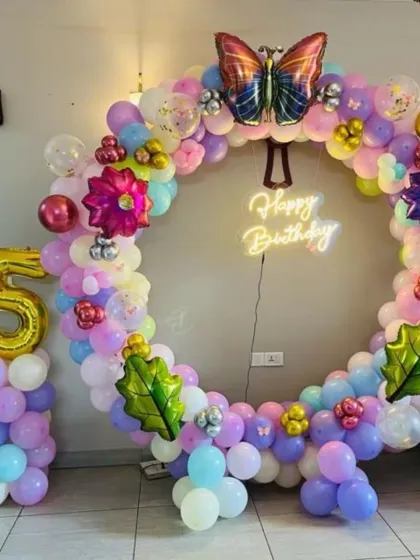 A colorful butterfly-themed 5th birthday party. This decoration features a circular balloon arch, a "Happy Birthday" neon sign, and a large number '5' foil balloon.