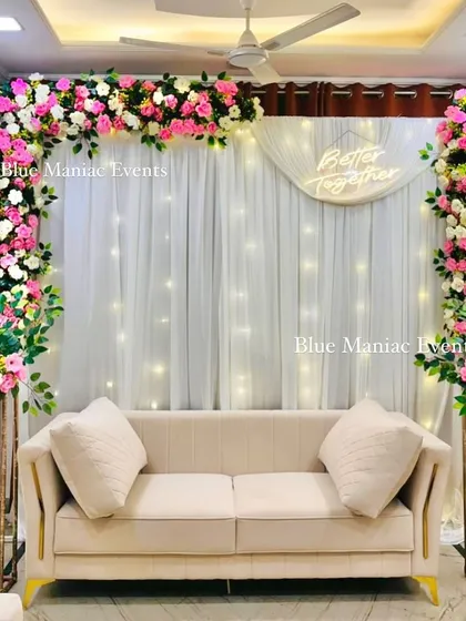 A beautiful home engagement setup with a rectangular frame of pink and white flowers. The design includes a 'Better Together' neon sign and matching floral stands for a complete and polished look.