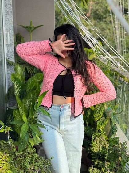 A chic and simple pink tie-front cardigan with a contrasting black trim. This lightweight piece is perfect for layering over a top or dress for a feminine and stylish look.