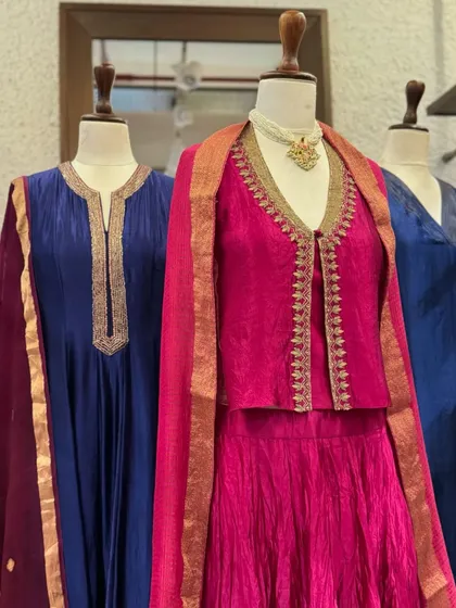 A close-up on the fuchsia jacket set, highlighting the delicate gold trim and the crushed texture of the skirt.
