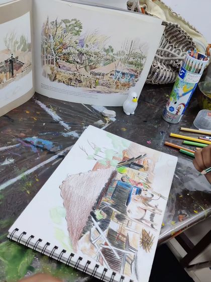 A young student works on a detailed landscape drawing with color pencils, learning to recreate a complex scene from a reference photo.