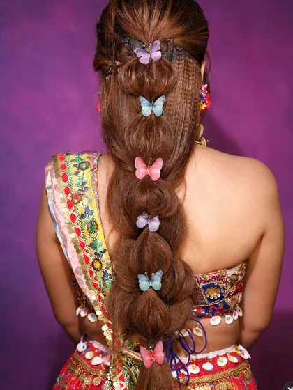 A modern take on a traditional braid. This bubble braid is accented with crimped hair textures and colorful butterfly clips, making it a trendy and eye-catching choice for a Sangeet or cocktail party.