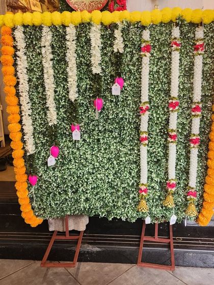 A beautiful Ganpati backdrop made with a green artificial leaf wall and decorated with white and yellow floral garlands. This creates a fresh, natural look for your festival setup.