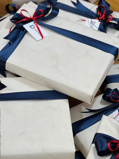 A corporate gift order for Unilight. The presents are wrapped in a subtle white marble-patterned paper and secured with a navy blue satin ribbon, featuring a custom tag with the company's logo.