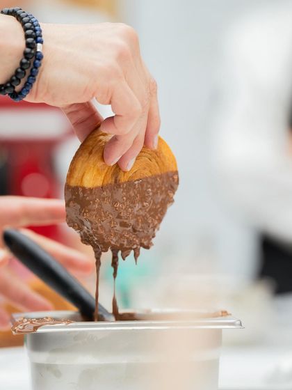 A croissant getting a generous dip in a rich chocolate-hazelnut coating. Guest chefs often bring their unique twists to classic pastries.