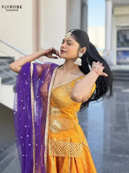 A close-up of this gorgeous orange lehenga, highlighting the unique blouse design and the contrasting purple net dupatta. A perfect look for a wedding guest.