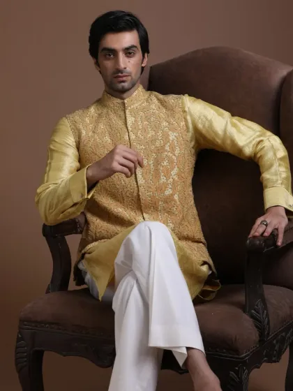 A proud reflection of culture and identity. This golden Nehru jacket, rich with tonal embroidery, is paired with a silk kurta and white trousers. It is a regal and confident look for any grand celebration.