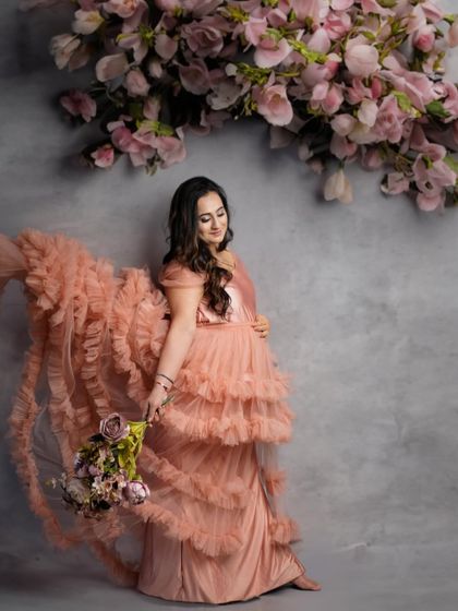 A graceful portrait of a mother-to-be in a flowing pink gown, surrounded by hanging flowers for a magical touch.