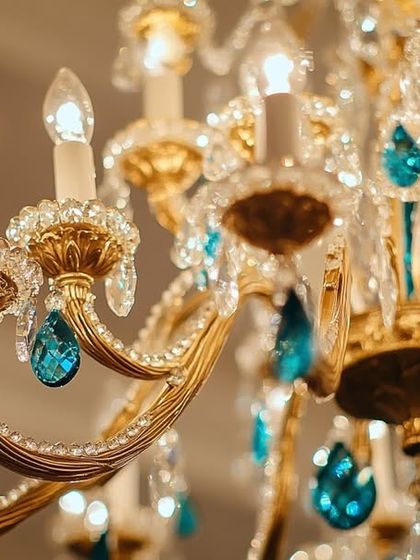 A close-up view of a classic gold and crystal chandelier, highlighting the intricate craftsmanship and the vibrant teal accents. This is a true masterpiece, designed for homes that deserve more than just light.