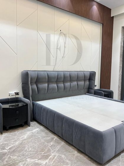 This elegant grey velvet bed features a tufted, winged headboard and a matching upholstered frame. It is paired with a unique fluted bedside table with a black glass top, combining classic comfort with modern details.