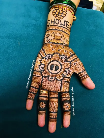 A beautiful and symbolic baby shower mehendi. The central mandala features tiny baby footprints, with the word "Shower" written on the wrist.