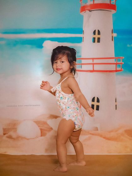 Ready for summer with this fun beach-themed studio shoot. The little girl in her swimsuit poses in front of a lighthouse backdrop, looking like a true beach bum.