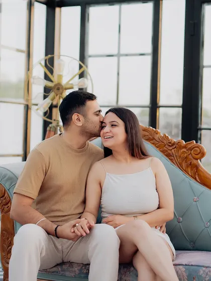 A sweet forehead kiss captured during an indoor session. The elegant glasshouse setting with vintage furniture provides a sophisticated and romantic atmosphere.
