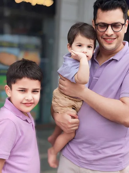 A father and his two sons in matching lavender shirts. This series captures their different personalities, from the curious toddler to the composed older brother.