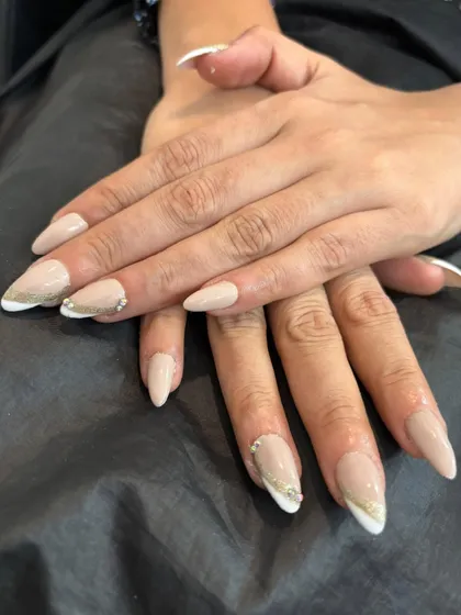 A modern twist on a timeless classic. These almond-shaped nail extensions feature a clean French manicure, elevated with a delicate gold line and a few sparkling rhinestones for a touch of elegance.