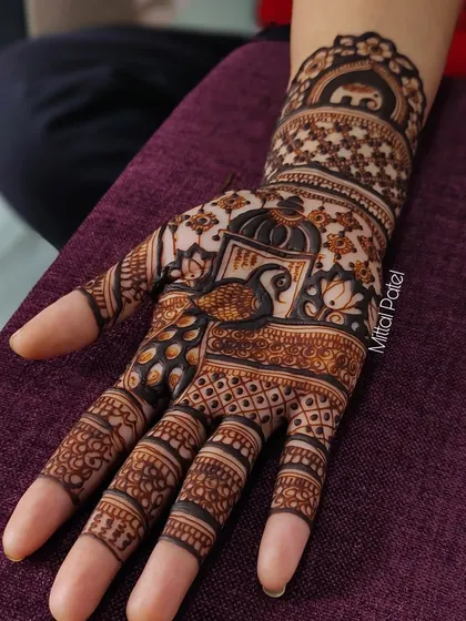 A close-up of a single hand, focusing on the detailed peacock figure within an ornate frame.
