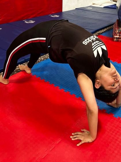 An adult student demonstrates an advanced backbend variation, touching her head to her feet. This level of flexibility is achieved through consistent and safe practice.