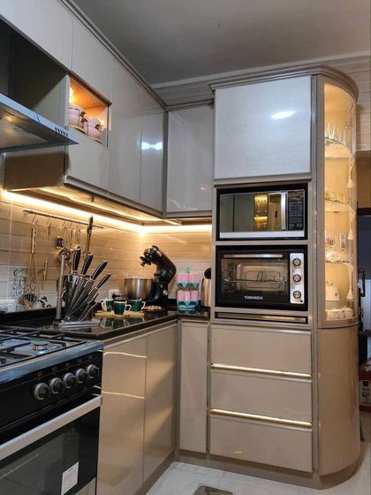 A close-up of a well-organized kitchen corner. This design showcases smart storage solutions, including a dedicated unit for a microwave and oven, and a curved glass display cabinet for an elegant touch.