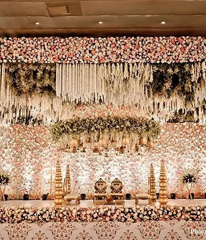 A spectacular, wall-to-wall floral stage we created for a grand Indian wedding reception. The backdrop features a dense arrangement of white and pink flowers with hanging tuberose strings, showcasing our capability for large-scale floral installations.