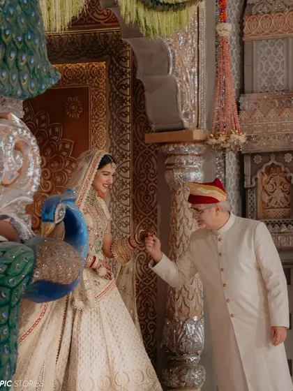 A beautiful, candid moment between Radhika and her father. The gentle interaction and shared smile amidst the grandeur of the temple setting highlight the deep, personal connections that are at the heart of every wedding.