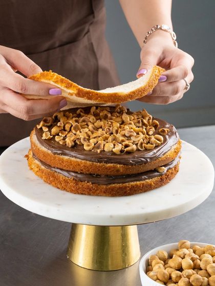 We believe in being generous with our toppings. Here you can see us layering our Hazelnut Divine cake with plenty of roasted hazelnuts for that perfect crunch and flavour.