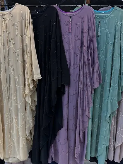 A rack of flowy, batwing style abayas in a rainbow of soft colours. The delicate embroidery on the chiffon fabric makes them light, airy, and beautiful.