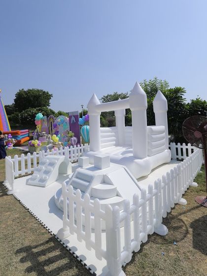 An all-white bouncy castle provides endless fun for kids at this outdoor carnival. The surrounding picket fence ensures a safe play zone while maintaining a clean, aesthetic look.