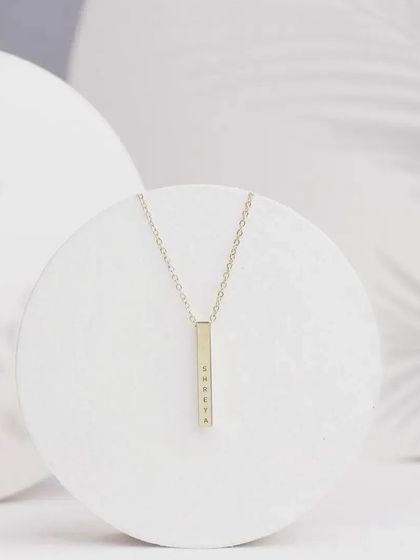 A minimalist product shot of a gold bar pendant engraved with 'Shweta'. The clean, white background emphasizes the simplicity and elegance of the design.