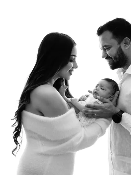 A classic black and white portrait of new parents admiring their baby. The high-contrast lighting creates a dramatic and timeless feel, focusing purely on their connection.