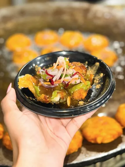 A hand holds up a serving of my Nawabi Tikki Chaat against the backdrop of the sizzling tawa. This captures the fresh, made to order nature of my live chaat stations.