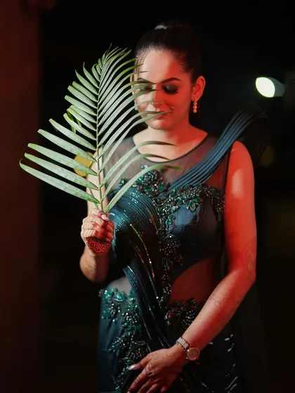 An elegant and moody solo portrait of the bride-to-be. The creative use of a palm leaf and soft red lighting adds an artistic touch, highlighting her grace and anticipation before the wedding.