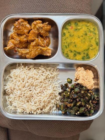 A wholesome meal of brown rice, chicken curry, dal, sautéed okra, and a side of pudi.