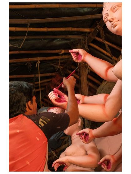 An artist delicately paints the hands of a Durga idol, a crucial step in bringing the divine figure to life before the festival begins.