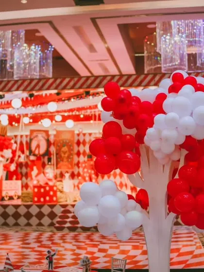 A wide shot of the circus stage, showing the vibrant red and white color scheme, balloon decorations, and checkered flooring. I design the entire space to feel like you've stepped right under the big top.