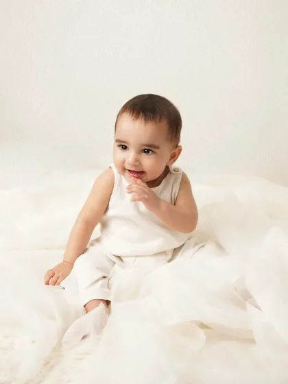 A sweet, shy smile from the baby boy, sitting amongst soft white tulle. The simple, angelic setup is perfect for capturing their innocence.