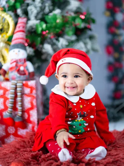 Little Ms. Claus is ready for Christmas. The festive red outfit and snowman prop create a classic holiday portrait.