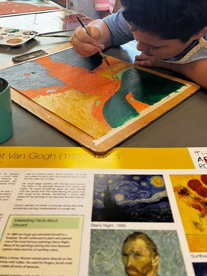 A student works on his Van Gogh-inspired painting, focusing on capturing the texture and movement of the cypress trees.