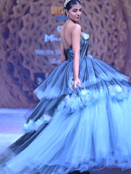 The back of this tiered tulle ball gown features a delicate halter neck and a sweeping train, creating a dramatic and unforgettable exit on the runway.