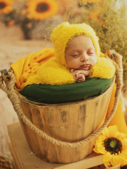 A bucket full of sunshine. This newborn, dressed in a fuzzy yellow outfit, sleeps soundly in a rustic wooden bucket surrounded by bright sunflowers.