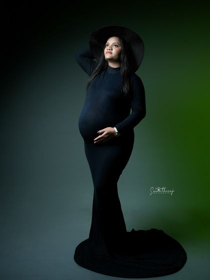 A powerful and stylish portrait of a mother-to-be in a black gown and hat. The dramatic lighting and her confident pose create a high-fashion, iconic look.