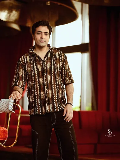 A portrait of actor Abir Chatterjee during a shoot for Anandalok magazine. The warm, ambient lighting of the location complements his patterned shirt, creating a relaxed yet sophisticated look for the editorial feature.