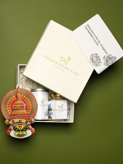 An angled view of the custom Taj Malabar Onam hamper, showing the branded box, welcome card, and the traditional Kathakali decor piece.