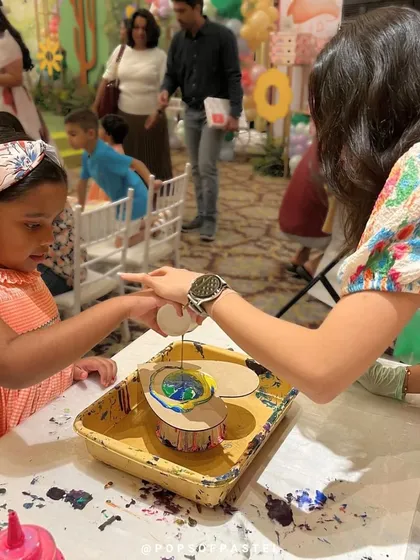 An instructor guides a young artist's hand as she pours paint, making our workshops accessible and fun for everyone, regardless of age.