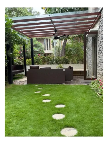 A view of the outdoor living area at Chaithanya Samarpan, with a lush lawn leading to a covered patio. The stepping stone pathway invites movement through the space, connecting the different zones of the garden.