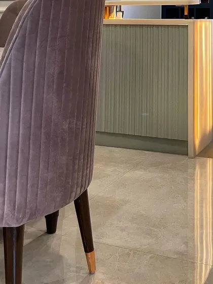 This image highlights the beautiful glow of the backlit Onyx bar counter, seen from behind a plush velvet dining chair. The light reflects off the polished floor, adding to the room's luxurious ambiance.