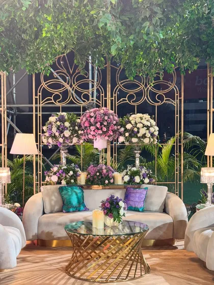 Spelling comfort and luxury with these gorgeous seating corners. Nestled under a canopy of lush greens and accented with purple florals, these spaces are both elegant and inviting.