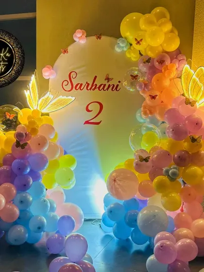 A colorful butterfly-themed second birthday. This setup uses a simple white backdrop to make the rainbow-colored balloon arch pop, accented with beautiful light-up butterfly props.