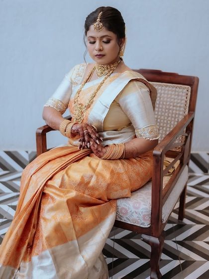 A full-length portrait of the mother seated gracefully in a chair. Her beautiful orange and white silk saree and the modern patterned floor create a stylish composition.